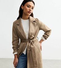 Beige, Wildleder-Trenchcoat mit tailliertem Gürtel, eingeschnittenem Kragen und langen Ärmel. Über einem weißen Oberteil getragen und mit blauen Jeans kombiniert.