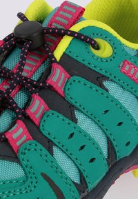 Sapatilha desportiva com um upper em malha teal, detalhes em preto, riscas rosa e pormenores em amarelo. Possui um sistema de atacadores rápidos e buracos de ventilação.