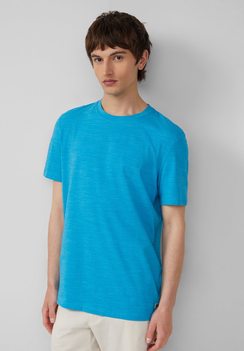 Niebieska koszulka z krótkim rękawem, wykonana z lekkiego materiału o teksturowym wykończeniu, okrągły dekolt, z delikatnym wzorem melanżowym oraz małą metką z logo u dołu.