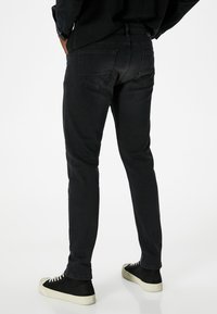 Jeans de denim negro con un corte ajustado, diseño de cinco bolsillos y bolsillos traseros cosidos. Combinados con zapatillas altas negras con suelas blancas.