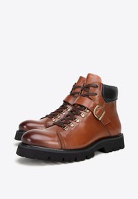 Botas de senderismo de cuero marrón con punta redondeada, tobillo acolchado, ojales de metal, diseño con cordones y un acento de cuero negro en el cuello.