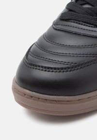 Μαύρο δερμάτινο αθλητικό παπούτσι με υφή στην επιφάνεια, ραφές και σόλα από καουτσούκ σε χρώμα γκαμ. �Κοντινή άποψη του τμήματος των δακτύλων.