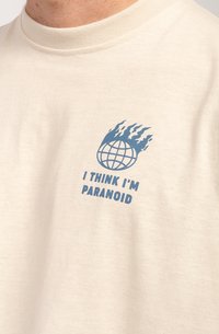 Cream-colored cotton t-shirt with a round neckline featuring a blue graphic of a globe with flames and the text "I THINK I'M PARANOID."