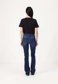 Black short-sleeve t-shirt paired with dark blue flared jeans featuring five pockets and contrasting stitching, viewed from the back.