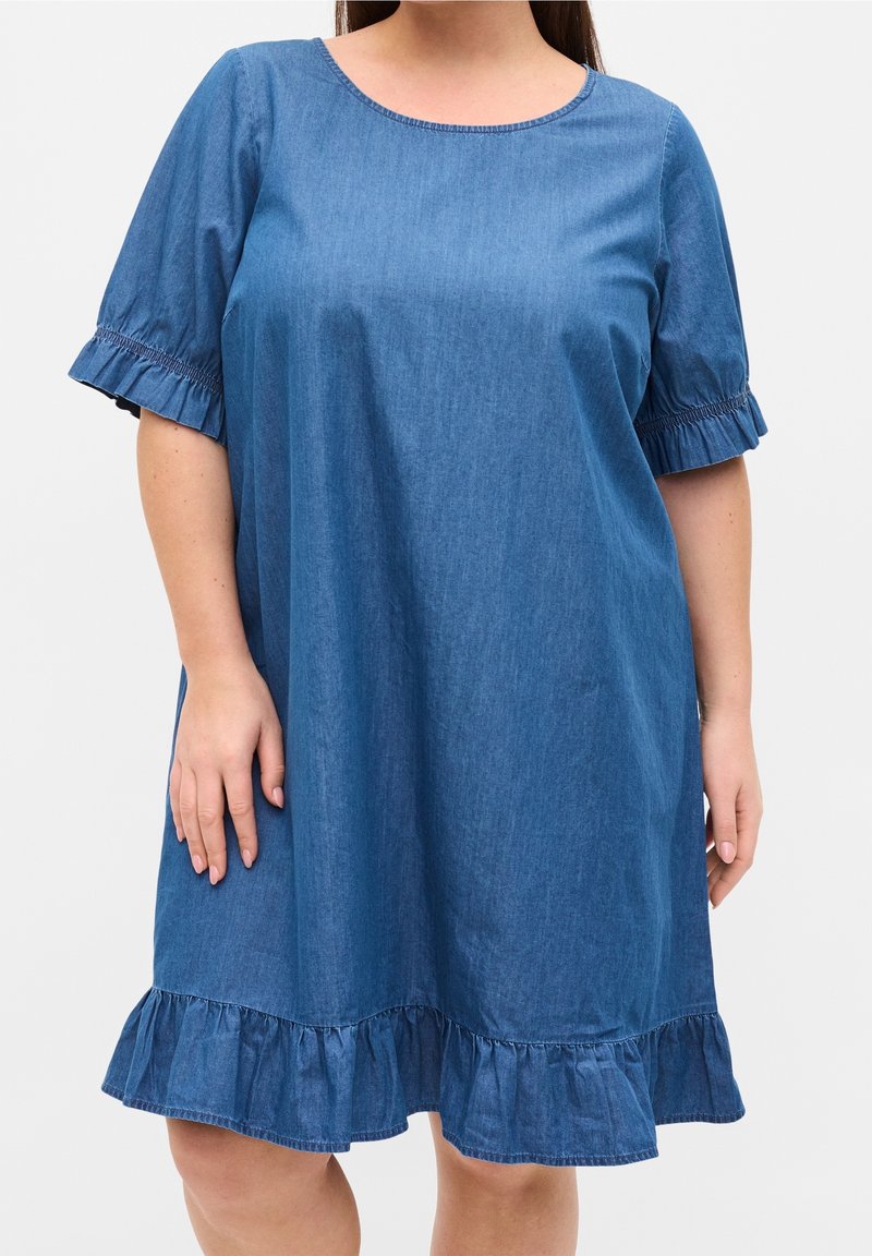 Vestido de mezclilla con cuello redondo, mangas cortas con volantes y dobladillo con volantes. La tela es de un color azul medio sólido con una textura suave.
