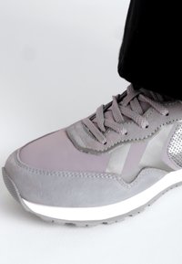 Scarpa da ginnastica grigia caratterizzata da un mix di materiali lisci e testurizzati, con suola bianca, lacci grigi e un pannello in rete metallica.