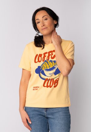 Geel katoenen t-shirt met "COFFEE CLUB" graphic met een croissant en koffie kop ontwerp in blauw en rood. Korte mouwen, ontspannen pasvorm.