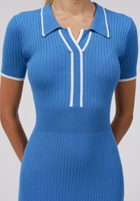 Abito blu lavorato a maglia con texture a coste, maniche corte e dettagli color bianco sul colletto. Presenta una scollatura a V e una silhouette aderente.