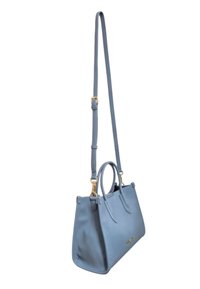 Borsa in pelle blu con dettagli in oro, doppi manici superiori e tracolla removibile. Texture liscia, forma strutturata, design minimale.