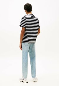 Czarny i szary w paski t-shirt z krótki rękawem noszony z jasnoniebieskimi dżinsami. Model tyłem, podkreślający wzór koszulki i jej luźny krój.