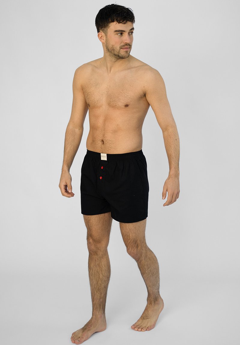 Shorts en coton noir avec un taille élastique, comportant deux boutons rouges à l'avant et un design simple.