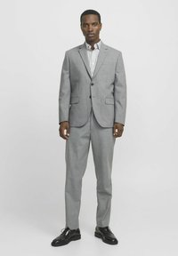 Pilka kostiumas su pritaikytu siluetu, dviejų mygtukų švarkas, įpjovos tipo apykaklė ir tiesaus kirpimo kelnės. Baltas ir pilkas dryžuotas marškinys, juodi aukšti batai.