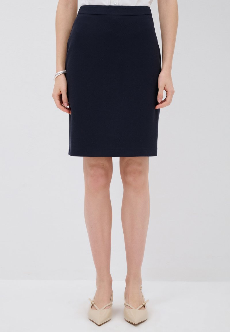 Sininen lyhythihainen hame, joka on valmistettu teksturoidusta kankaasta, keskikorkealla vyötäröllä ja sileä vyötärö, yhdistettynä beigeihin teräväkärkisiin korkokenkiin.