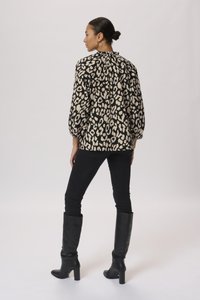 Blusa leopardata nera e beige con colletto alto, maniche a sbuffo e dettaglio arricciato nella parte posteriore, abbinata a jeans skinny neri e stivali neri alti.