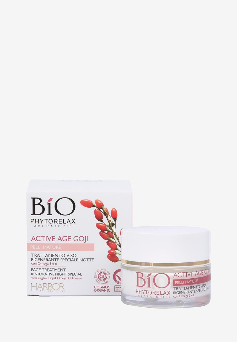 Goji ansiktskräm i en genomskinlig burk med ett vitt lock, placerad bredvid en vit låda med röda gojibär och rosa accenter.