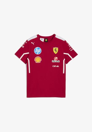 Czerwona koszulka wyścigowa Ferrari z logo Puma, sponsorami Shell, HP, UniCredit i Ceva oraz żółtą tarczą Ferrari na klatce piersiowej i ramionach.