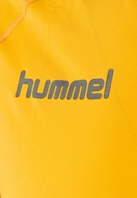 Gelbe Sportbekleidung mit einer weichen, glatten Textur und einem auffälligen grauen "hummel"-Logo aufgedruckt.