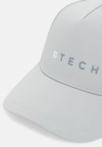 Gaiši pelēks cepures modelis ar strukturētu dizainu, gludu audumu, plakanu lodi un iegrieztu "B TECH" logotipu kontrastējošās krāsās.