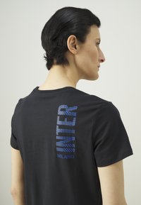 Čierne bavlnené tričko s krátkymi rukávmi, na zadnej strane s vertikálnym modrým prúžkovaným textom "INTER MILANO."