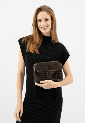 Bruine suède en faux-krokodillenleren handtas met een ritssluiting, met een vlakke voorflap, vastgehouden door een model in een zwarte gebreide jurk.