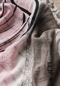 Patroon sjaal met lichtroze, zwart en beige tinten. Zachte, gestructureerde stof met bloem- en abstracte ontwerpen. Zichtbare stiksels en accenten.