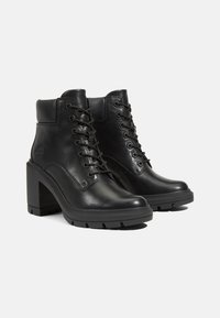 Botas de cuero negro hasta el tobillo con puntera redondeada, cordones en la parte delantera y tacón alto y grueso. Presentan una suela texturizada para mejor agarre.