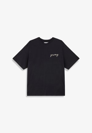Camiseta de algodón negra con mangas cortas, cuello redondo y texto blanco en cursiva "grmy" en el lado izquierdo del pecho. Diseño simple y sin adornos.