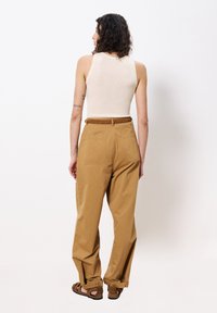 Beige geribbelde tanktop, gecombineerd met hooggewaaid, losse tan broeken. De outfit heeft een geweven bruine riem en sandalen met open tenen.
