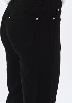Czarne dżinsy o dopasowanym kroju, z metalowymi detalami przy tylnej kieszeni oraz gładkim, teksturowanym wykończeniem.