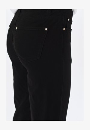 Czarne dżinsy o dopasowanym kroju, z metalowymi detalami przy tylnej kieszeni oraz gładkim, teksturowanym wykończeniem.