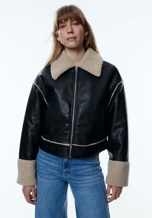 Zwarte leren cropped jack met een beige schapenvacht kraag en cuffs, voorzien van een ritssluiting aan de voorkant en zichtbare stikselaccenten.