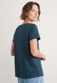 Tyrkysové bavlněné tričko s kulatým výstřihem a krátkými rukávy, s volným střihem a rovnými lemy, nošené s světle modrými džíny.