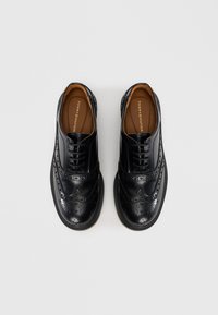 Black leather shoes with a brogue design, featuring decorative perforations, raised edges, and a rubber sole. Inside has a tan lining.