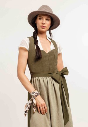 Abito verde oliva con un corpetto aderente, gonna in lino svasata e una cintura coordinata. Accessorio: una sciarpa a fantasia legata al polso. Cappello in feltro grigio.