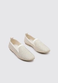 Zapatos blancos sin cordones con un diseño perforado y pequeños acentos en forma de diamante. Punta redondeada y suela de perfil bajo para un aspecto moderno.