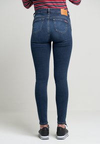 Mörkblå högmidjade skinny jeans med en läderlapp på baksidan och två bakfickor, tillsammans med svarta sportskor.