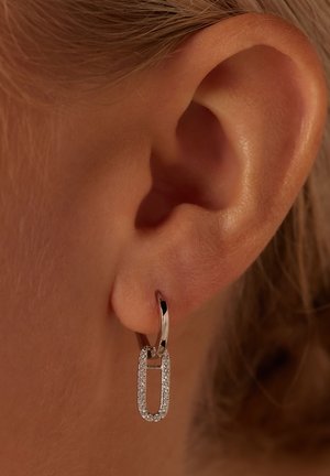 Silver hoop earrings in a paperclip shape, adorned with clear crystals along the edges, hanging from a small lever back.