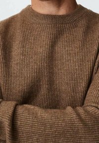 Maglione a coste marrone con scollo rotondo, tessuto testurizzato e vestibilità aderente, che mette in evidenza sottili variazioni di colore.
