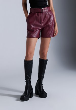 Burgundy faux leather high-waisted shorts with a belted waist, pleats, and black knee-high platform boots with chunky heels.