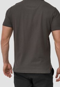 Polo gris foncé à manches courtes, texture lisse, col côtelé et fentes latérales à l'ourlet. Vue de dos montrant les coutures des épaules.