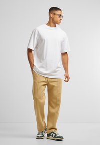 Witte katoenen T-shirt met korte mouwen, gecombineerd met beige joggingbroeken met zijnaad, en groene en witte sportschoenen.