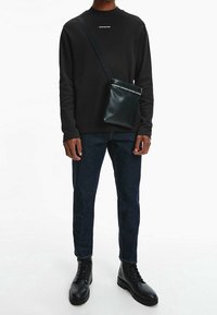 Svart sweatshirt med vit text, mörkblå jeans, svarta läderstövlar och en liten svart axelväska med kontrasterande remdetalj.