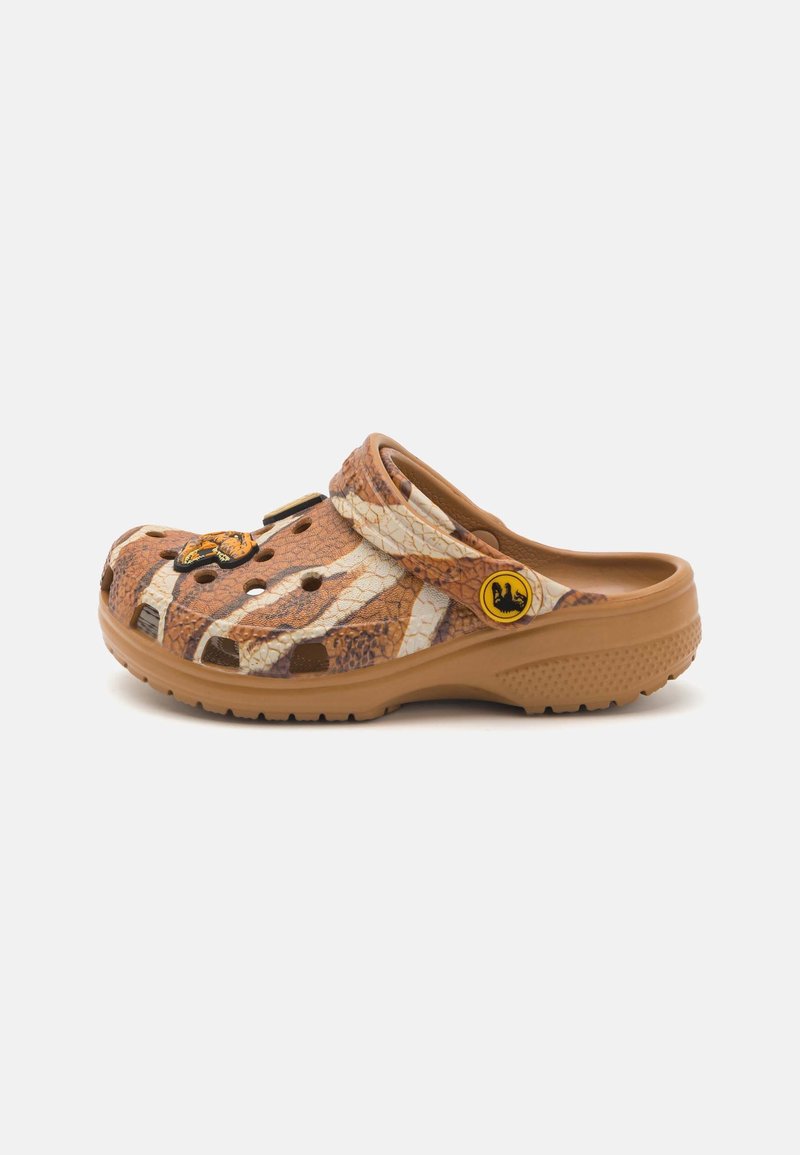 Sabot marron à enfiler avec imprimé animal beige et marron foncé, trous de ventilation et une bride avec un logo circulaire jaune sur fond blanc.