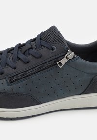Sneaker en bleu marine foncé avec cuir perforé, tige en mesh, lacets plats, détail de zip sur le côté et semelle en caoutchouc texturé blanche.