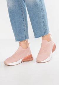 Vaaleanpunaiset neulottuja lenkkareita, joissa on hengittävä päällinen, valkoinen pohja ja läpikuultava, pehmustettu kanta. Lenkkareissa on helposti jalkaan sujautettava malli.