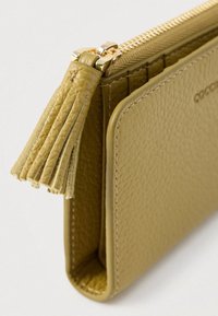 Beige textured leather wallet with tassel zipper pull and stitching details on a white background.