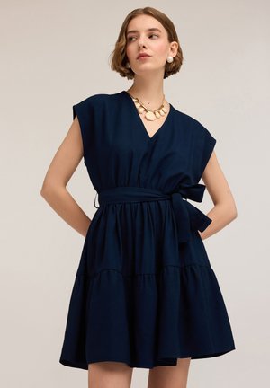 Abito di cotone blu navy con maniche corte, scollo a V, vita aderente e gonna a strati. Presenta una cintura con nodo in vita e una texture liscia.