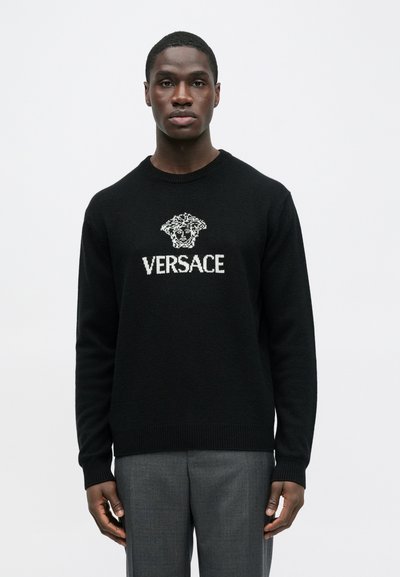 Černý pletený svetr s bílým vyšívaným logem Versace a motivem hlavy Medúzy na přední straně. Jednoduchý kulatý výstřih a dlouhé rukávy.