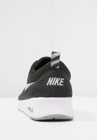 Svart Nike-sneaker med överdel i mesh, vit gummisula och kontrasterande grå detaljer. Inkluderar en dragflik med horisontella ränder.