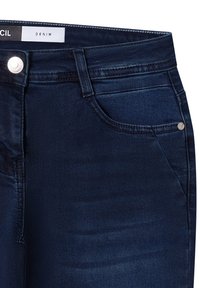 Jeans de denim azul oscuro con un diseño ajustado, que cuentan con una etiqueta en la cintura, bolsillos delanteros y un botón y acentos en tono plateado.